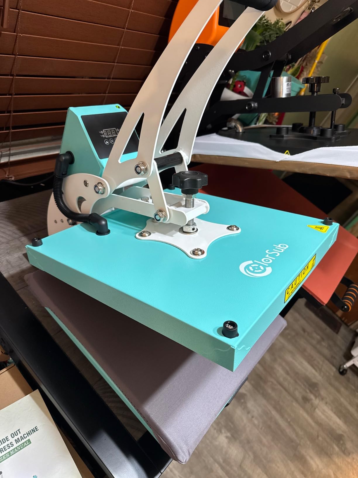Side view of a teal ColorSub 15 x 15 heat press in a home workshop